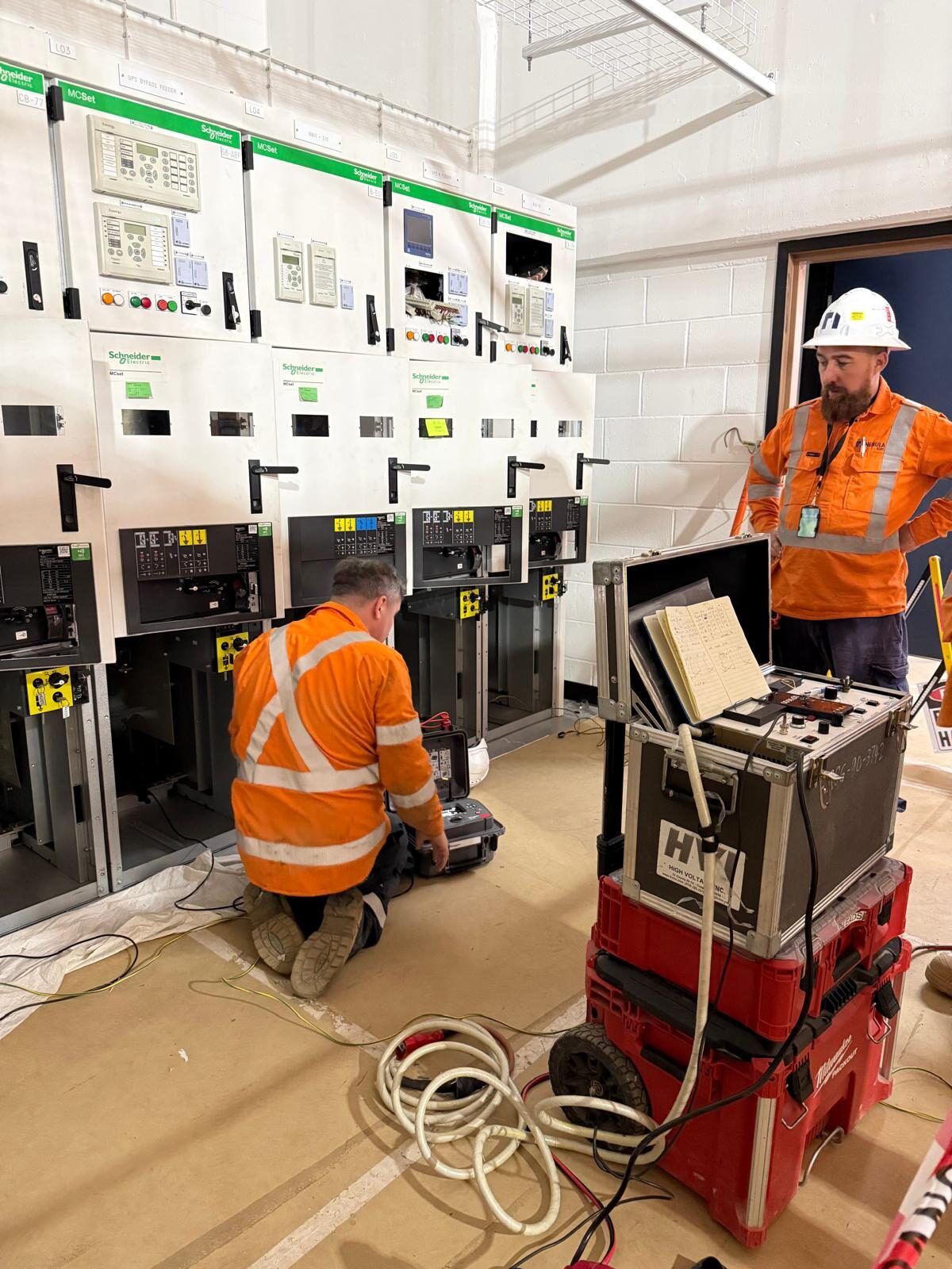 A Nebula technician kneeling at a switchboard with a secondary injection test set