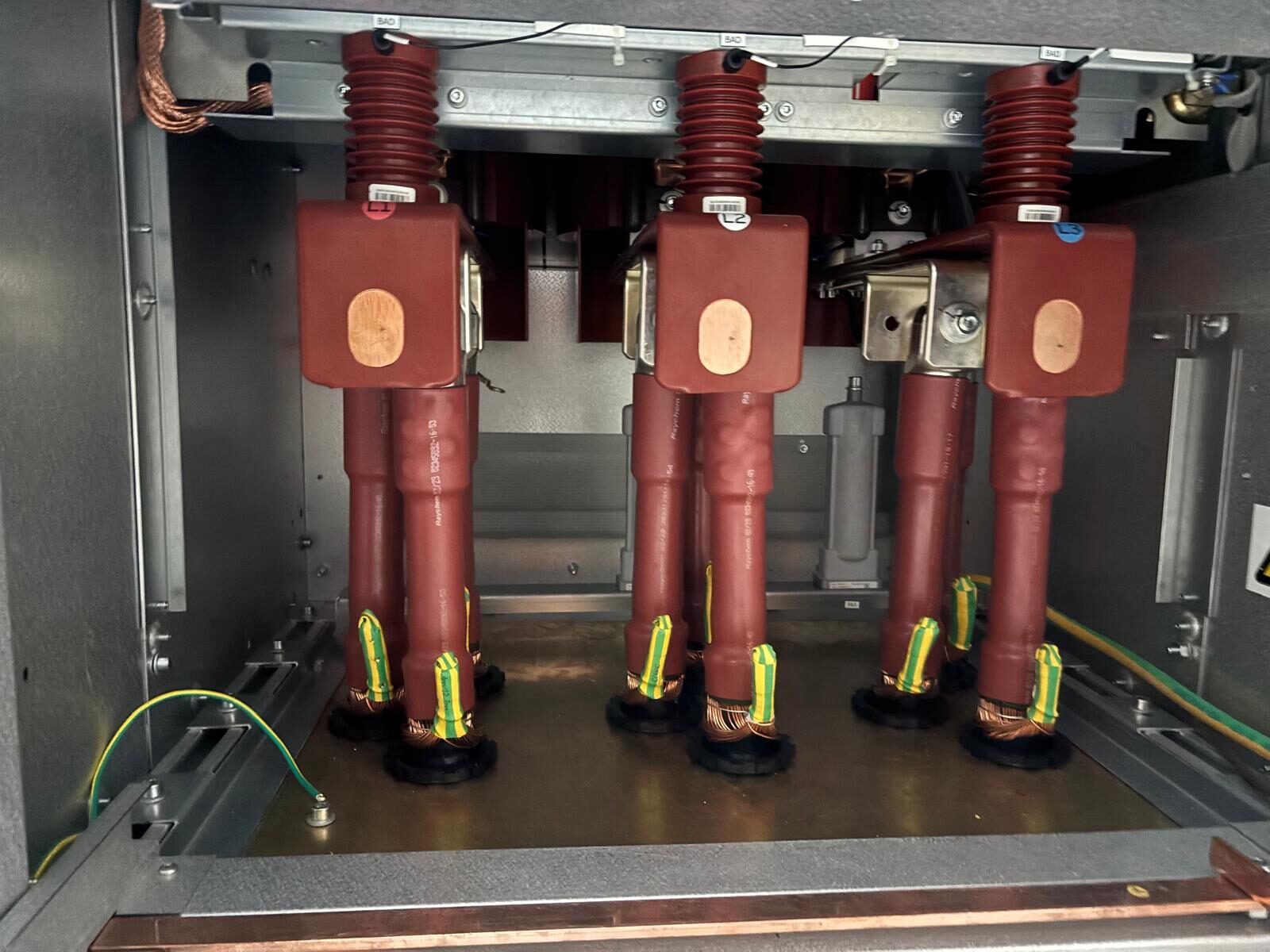 The interior of a switchgear cubicle, bushings and earth connections visible