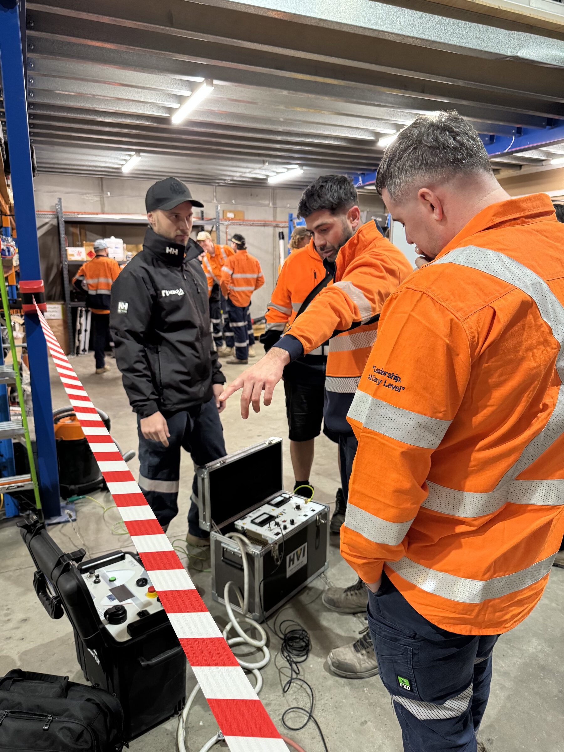 An instructor walking the crew through a test kit on the workshop floor, barrier tape across the bay
